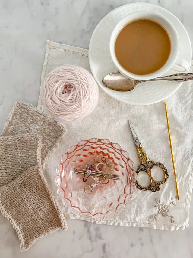 A top down shot of a collection of knitting tools, including scissors, stitch markers, and a crochet hook.