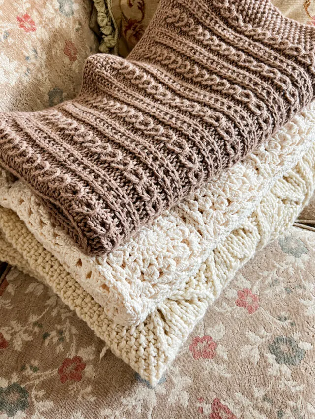 A pile of folded handknit and crocheted blankets.