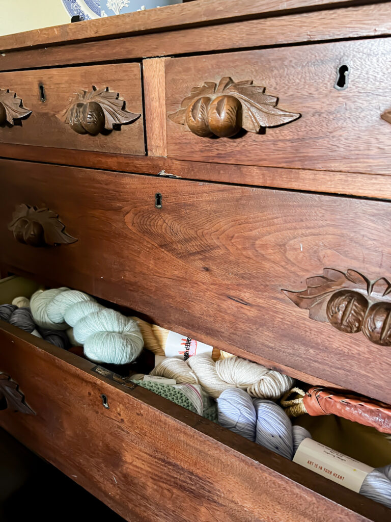 A drawer on an antique Eastlake dresser is slightly ajar, showing an abundant amount of yarn tucked inside.