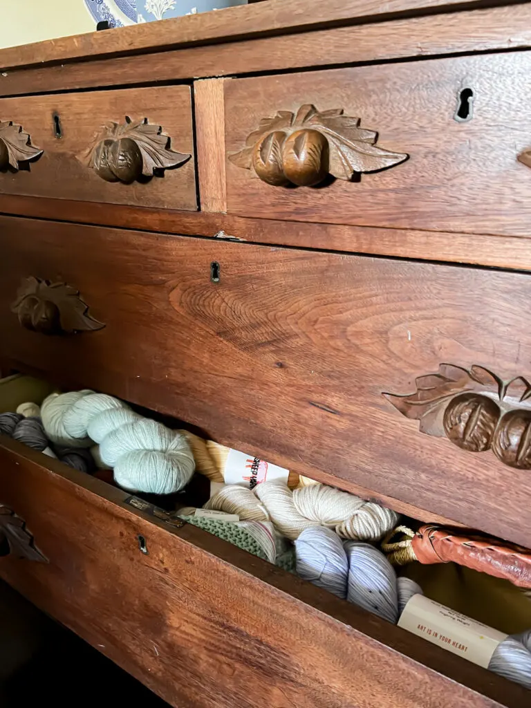 A drawer on an antique Eastlake dresser is slightly ajar, showing an abundant amount of yarn tucked inside.