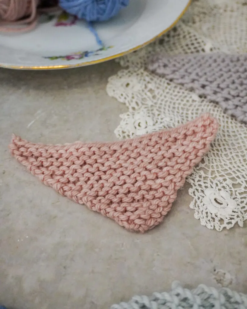 A close up on a pink mini shawl. This shows a triangle shawl cast on from the bottom point and shaped using one increase at the end of each right side row and at the end of each wrong side row.