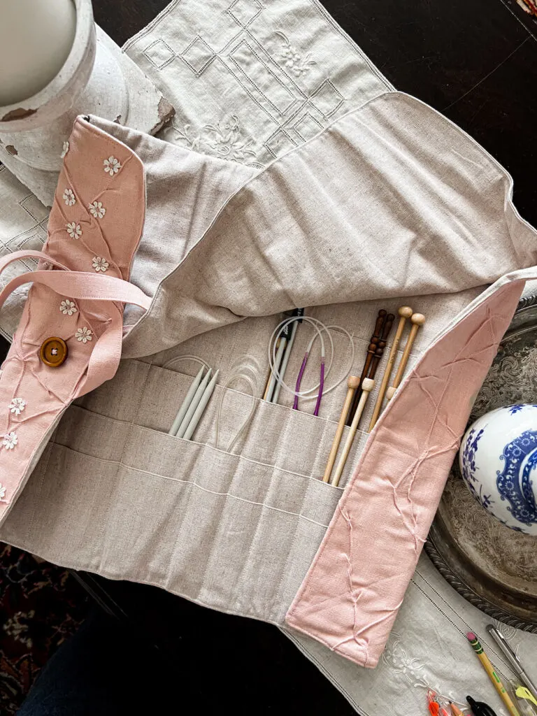 A pink needle roll is opened up to show the compartments full of knitting needles.