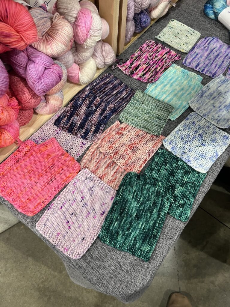 The swatch display at Wildstar Fibers, which featured both knit and crochet swatches. This shows swatches in hot pink, soft lavender, and rich forest green, plus several variegated colorways.