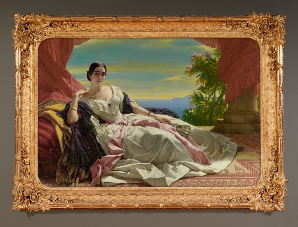 Description from the Getty Museum: In a daring pose reminiscent of harem scenes and odalisques, the princess Leonilla of Sayn-Wittgenstein-Sayn reclines on a low Turkish sofa on a veranda overlooking a lush tropical landscape. Only her unassailable social position made it possible for Franz Xaver Winterhalter to use such a sensual pose for a full-length portrait in Paris in 1843. Known for her great beauty and intellect, the princess is resplendent in a luxurious gown of ivory silk moiré with a pink sash around her waist. A deep purple mantle wraps around her back and falls across her smooth arms. Under carefully arched eyebrows, her heavy lidded eyes gaze languidly at the viewer while she artfully toys with the large pearls around her neck. Winterhalter contrasted sumptuous fabrics and vivid colors against creamy flesh to heighten the sensuality of the pose, the model, and the luxuriant setting.