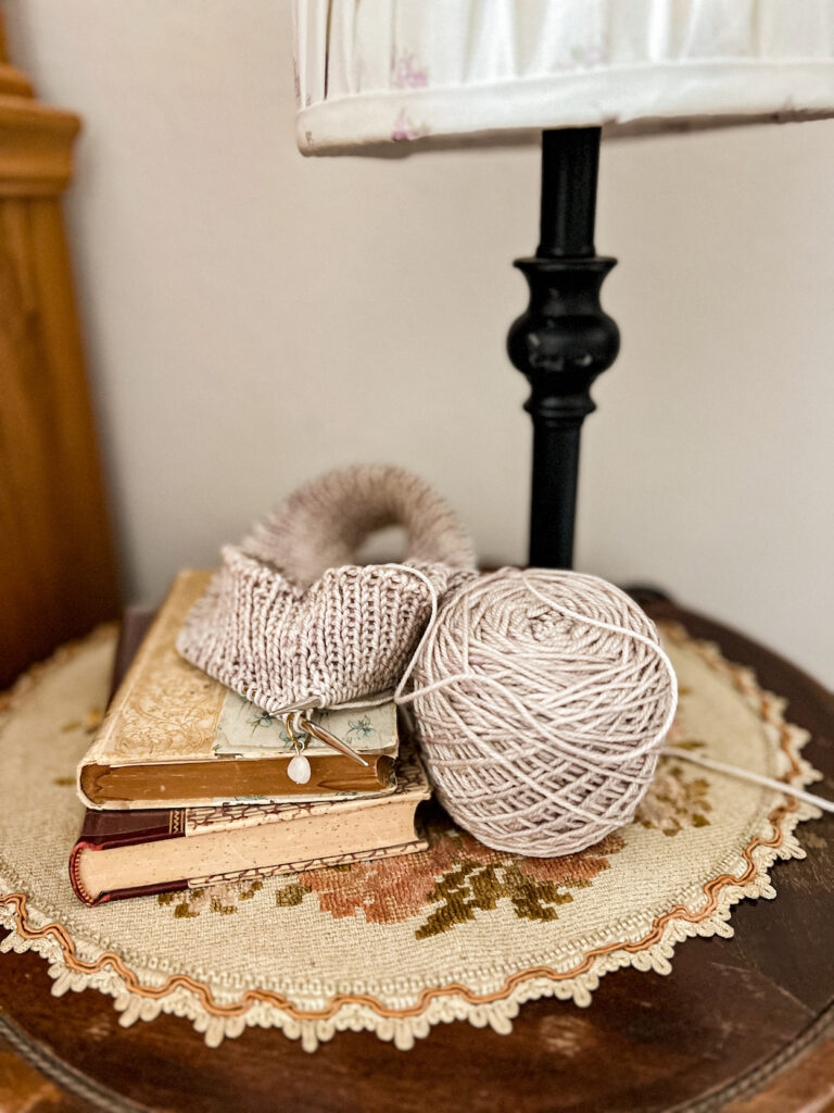 A tan knitting project in progress sits on a small stack of antique books.