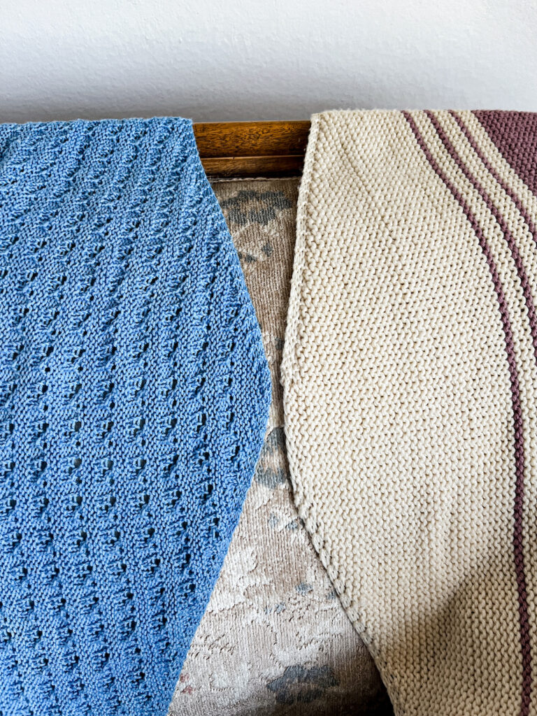 Two shawls are laid out on a vintage sofa with their cast-on edges in the middle. The shawl on the left, a blue lacy shawl, has a garter tab cast-on at the central peak. The shawl on the right, a white garter-stitch shawl with purple stripes, has a long-tail cast-on at the peak.