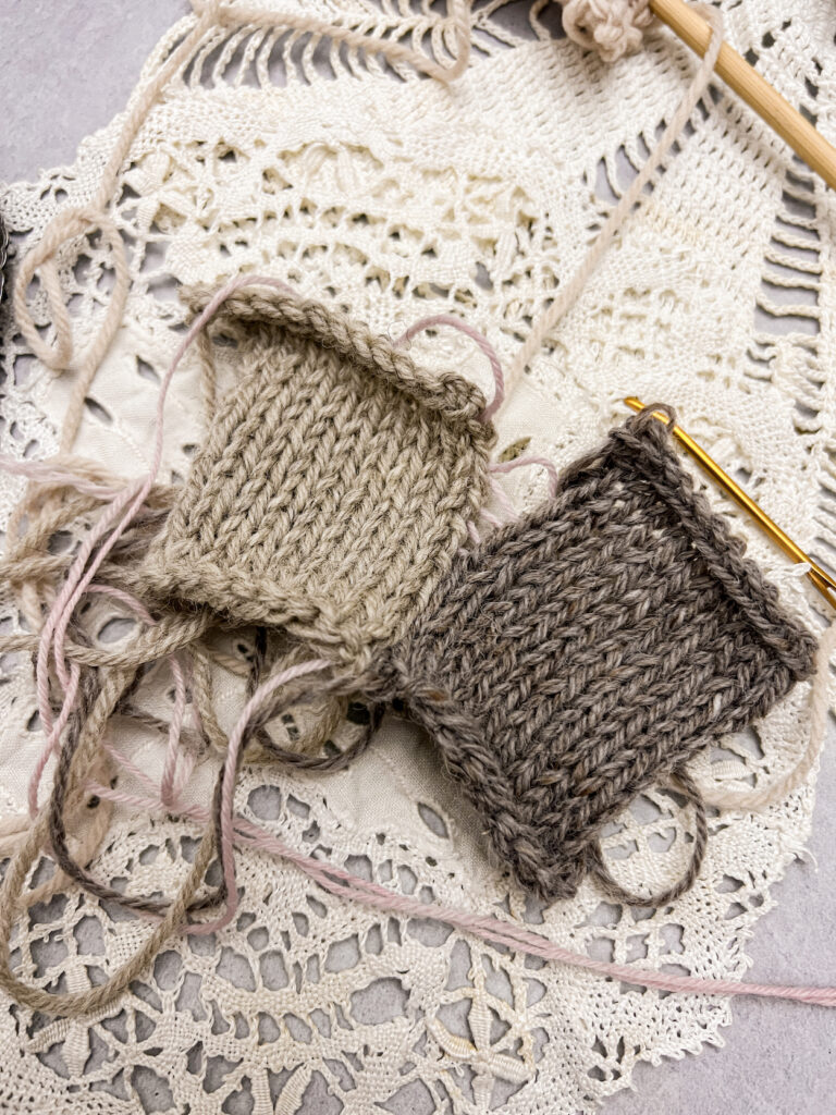 A pair of knit squares, one tan and one dark brown, are halfway seamed with the mattress stitch. At the bottom of the seam, the stitches have been pulled tight, but toward the top, the stitches have been left loose so the viewer can see the strands of pink yarn passing back and forth between the squares. The squares sit on top of a vintage doily.