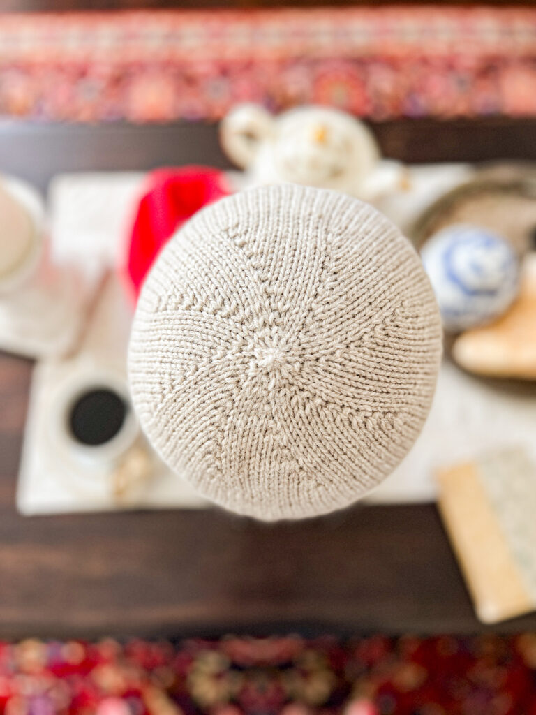 A top-down image of the crown of a tan knit hat showing spiraling kfb increases from the center of the crown.